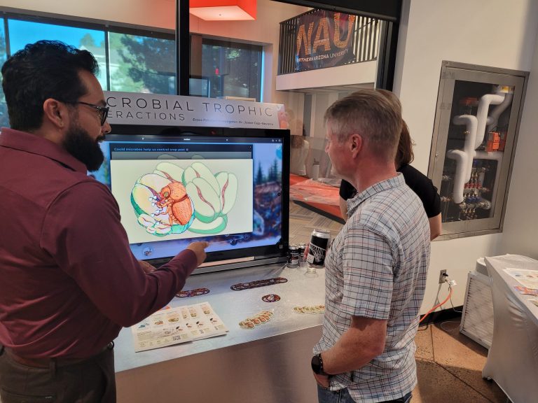 A researcher walking a guest through a lab diorama on a touch screen
